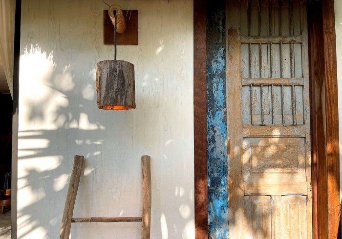 Puerta de madera y pared blanca con farol colgante, sombras iluminadas por el sol y una escalera apoyada contra la pared.