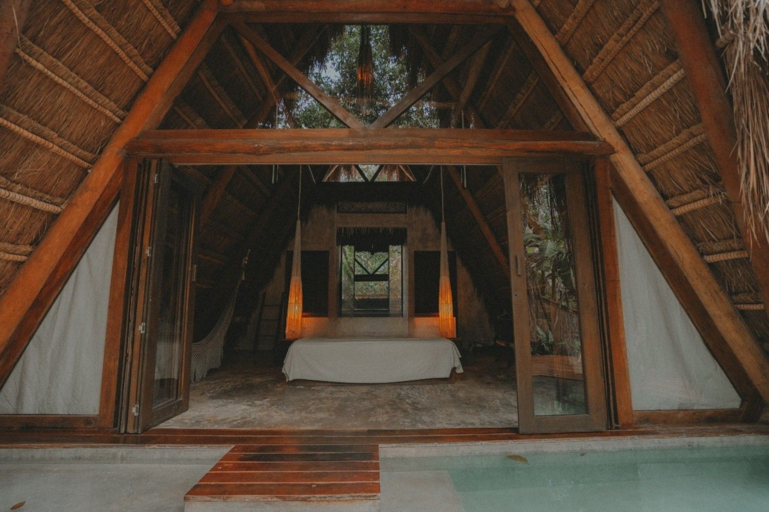 Interior de madera con estructura en forma de A, cama central y detalles en color naranja cálido en la parte trasera.