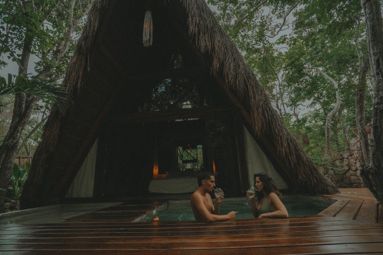 Dos personas se relajan en una piscina en una cabaña de la selva con árboles a su alrededor.