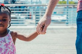 Adult holding a child’s hand on a boardwalk with blue railings in the background