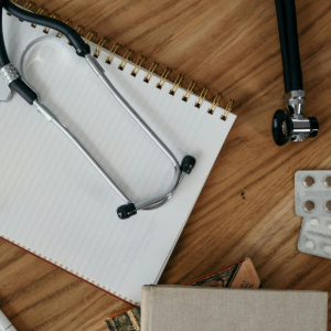 Notebooks and stationery on a wooden desk with a stethoscope and a pen, suggesting a study or work setup