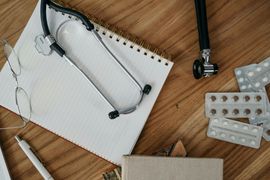 Notepad, stethoscope, earpiece, and blister packs on a wooden desk