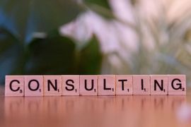 Wooden letter tiles spelling “CONSULTING” on a table with a blurred background