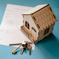 Wooden house model with keys on a blue surface beside an open document.