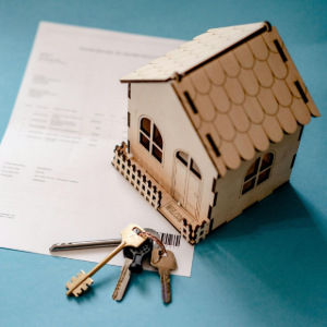 Wooden house model with keys on a blue surface beside an open document.