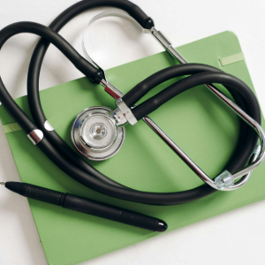 Black stethoscope on a green clipboard, with pen attached