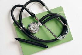 Black stethoscope on a green clipboard on a white background