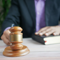 Judge’s gavel on a desk with a blurred lawyer in a suit holding a law book.