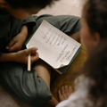 Hands around a paper checklist on a lap, with one person writing with a pencil.