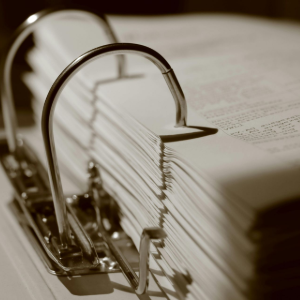 Sepia close-up of a metal paper clip holding a stack of white pages in a binder