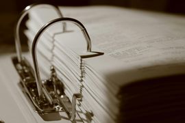 Sepia-toned close-up of a ring binder filled with papers on a desk