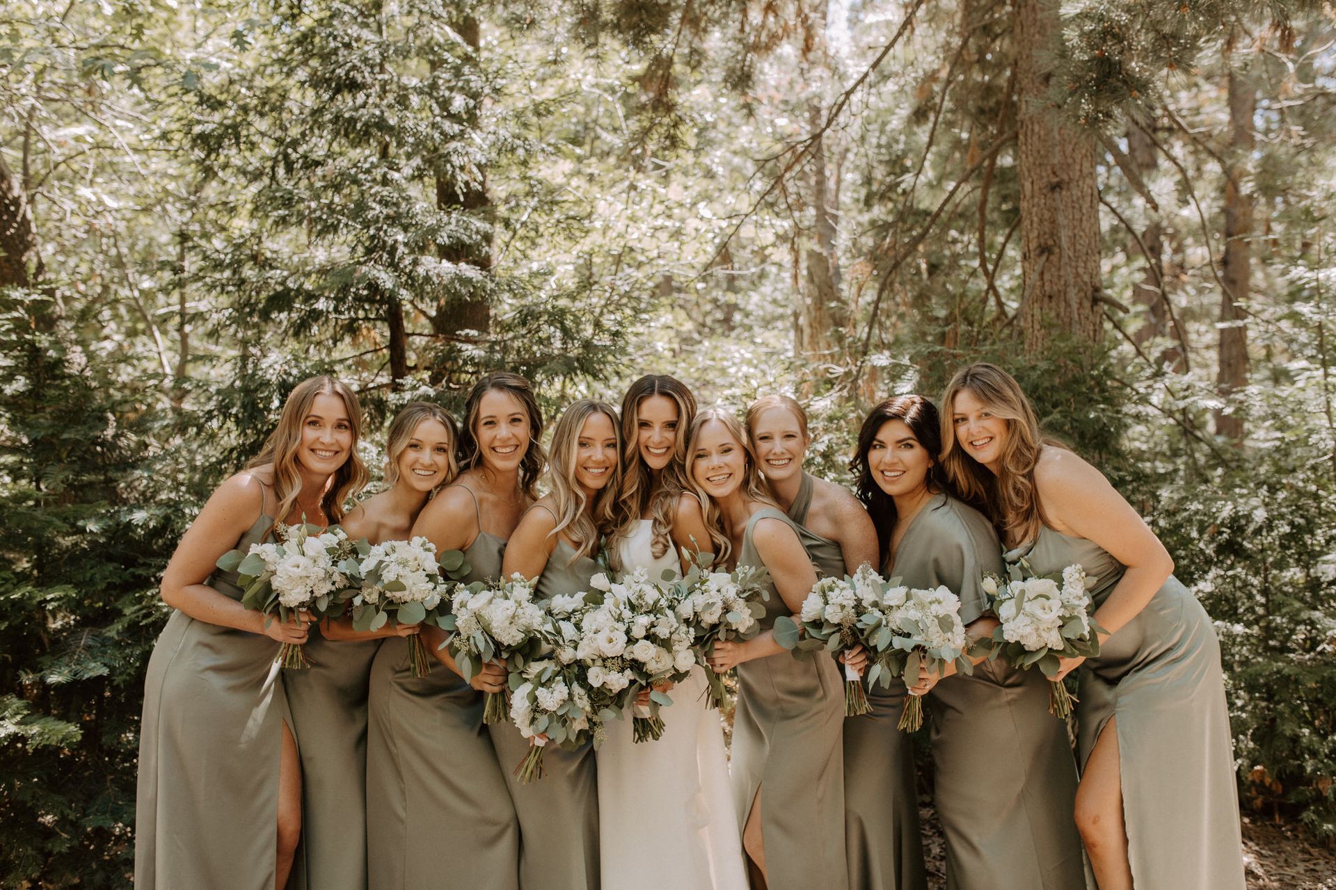 A bride and her bridesmaids are posing for a picture in the woods.
