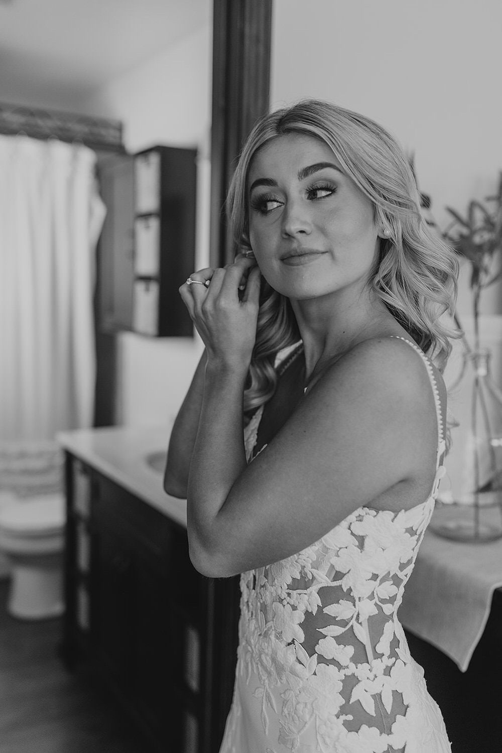 A black and white photo of a bride putting on her earrings.