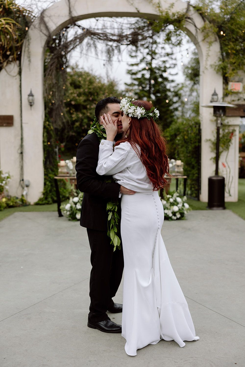 A bride and groom are kissing in front of a white building.