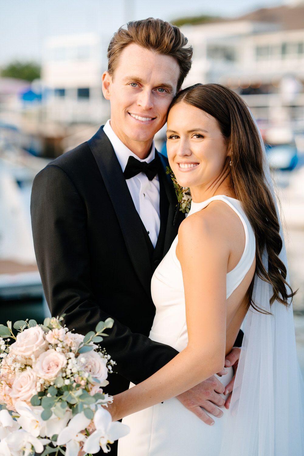 A bride and groom are posing for a picture in front of a boat. Orange county hair and makeup artist.