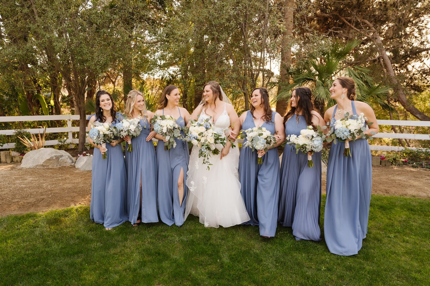 A bride and her bridesmaids are posing for a picture in the grass. Orange county hair and makeup artist.