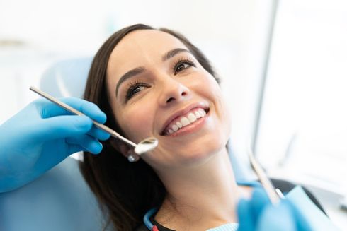 Donna sorridente sulla poltrona del dentista; la mano guantata del dentista tiene gli strumenti, esaminando i denti. Studio luminoso.