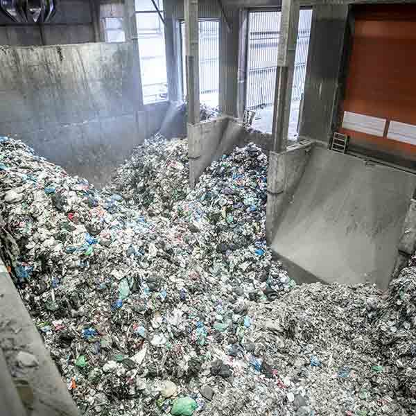 Large indoor waste facility with piles of mixed trash and sorting chutes under bright windows