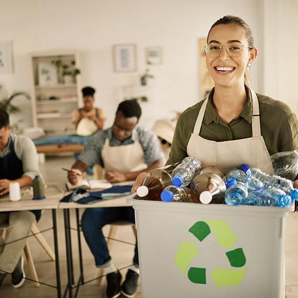 Woman smiling behind a recycling bin full of plastic bottles in a community cleanup setting