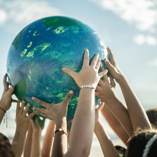 Hands lifting a large blue-green globe against a bright sky