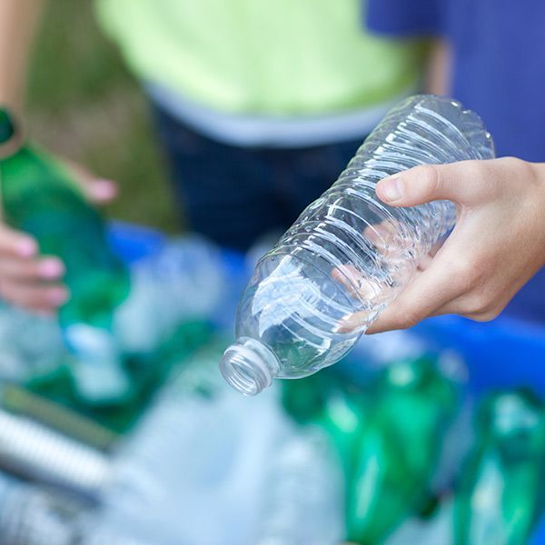 Hand holding an empty clear plastic bottle near a pile of recyclables