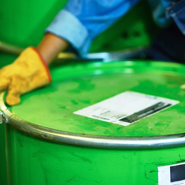 Gloved hand pushing a green metal drum with a white label on top