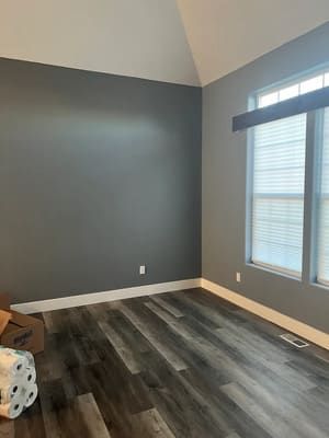 An empty room with hardwood floors , gray walls and two windows.