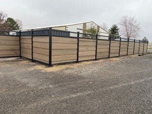 A wooden fence is sitting on the side of the road next to a building.