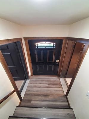 A hallway with a black door and stairs leading up to it.