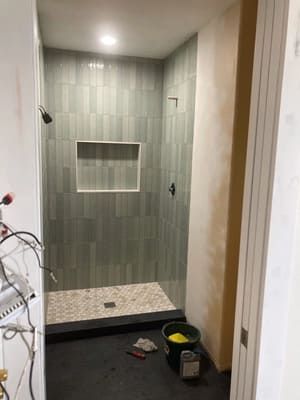 A bathroom with a walk in shower and a bucket on the floor.