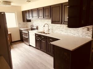 A kitchen with black cabinets , white appliances , a sink , and a refrigerator.