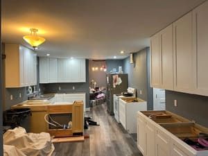 A kitchen under construction with white cabinets and hardwood floors.