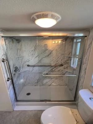 A bathroom with a toilet , shower , and sliding glass door.