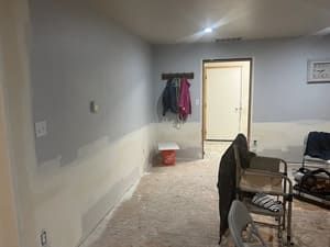 A room with a carpeted floor , a chair , a table and a door.