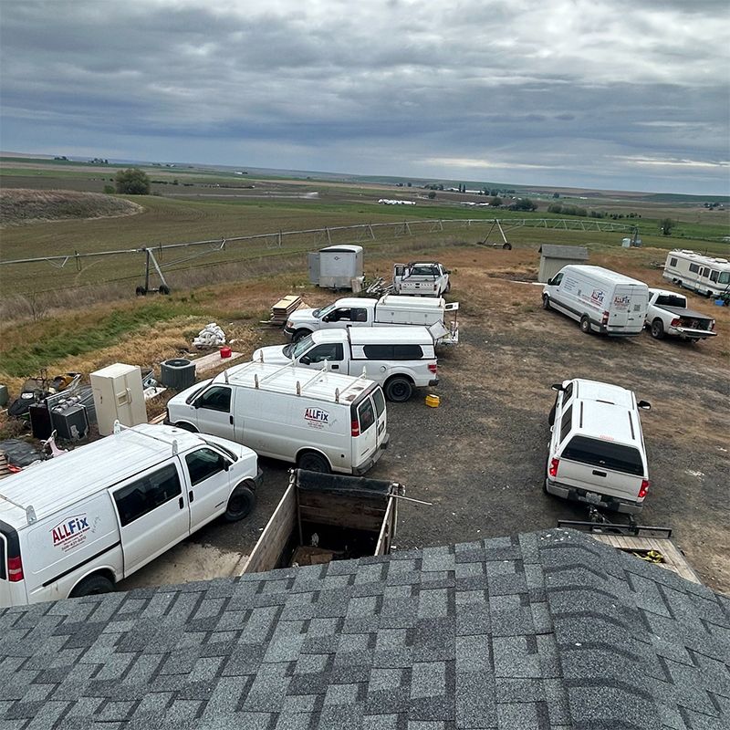 View from a roof with multiple white vans and trucks parked on a dusty lot, overlooking a vast field under a cloudy sky.