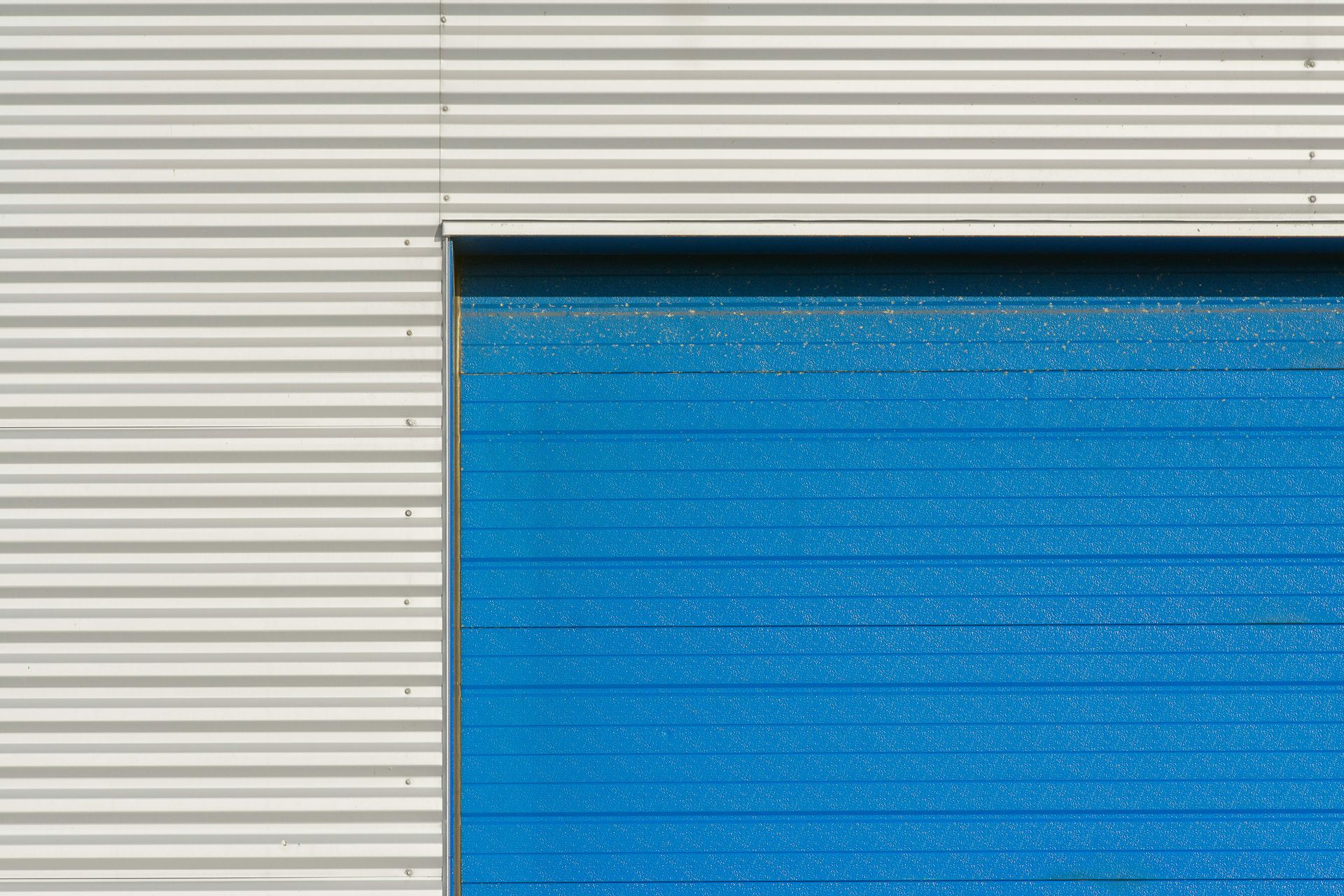 A blue garage door is sitting next to a white wall.