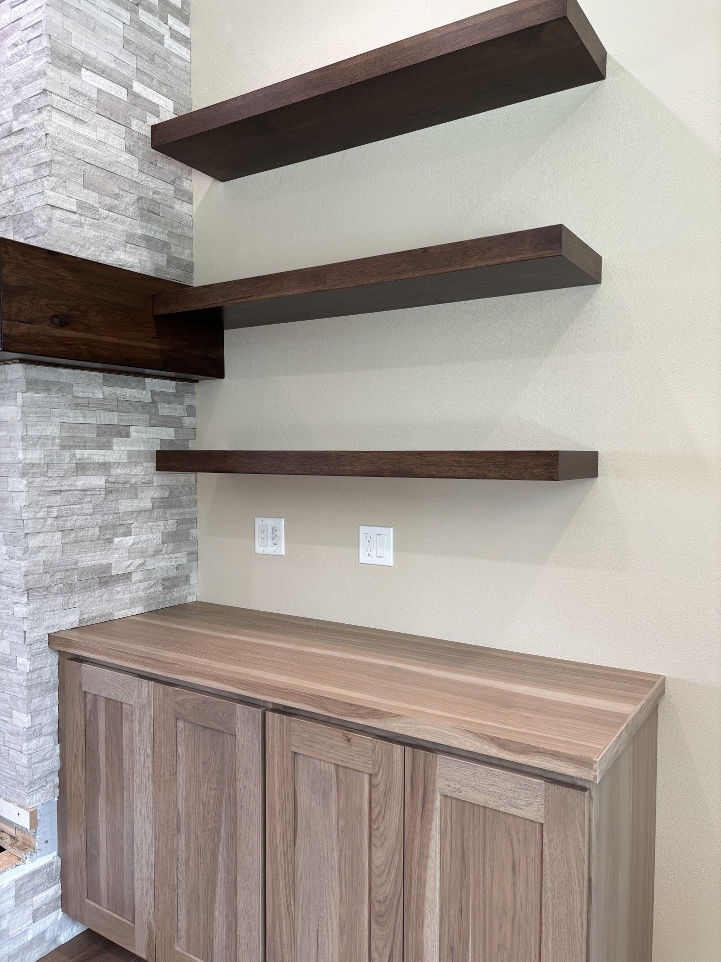 Built-in shelves above a cabinet with a wooden countertop. Shelves are brown against beige wall with stone accent.