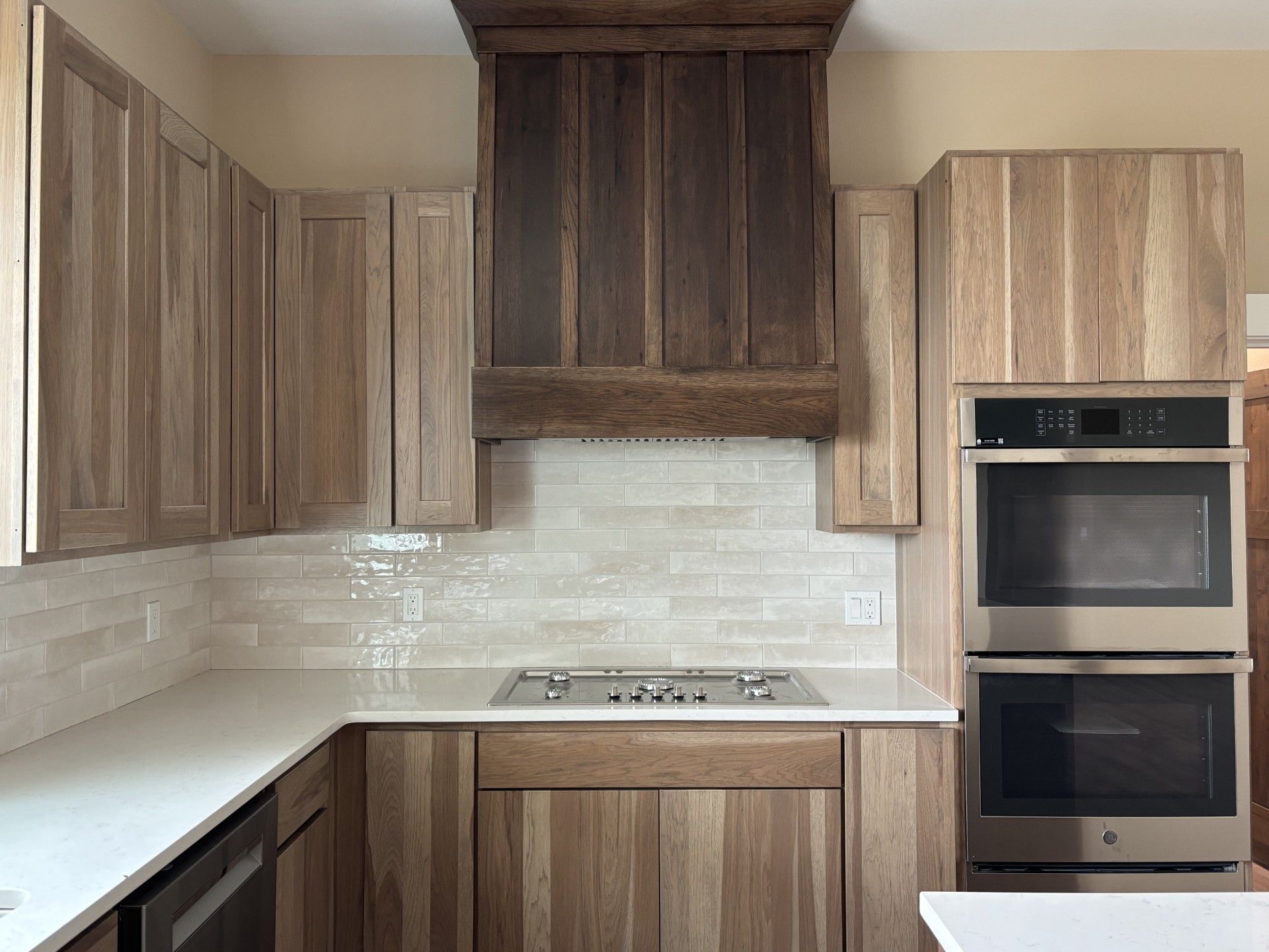 Kitchen with light wood cabinets, a dark wood range hood, white countertops, and a double oven.