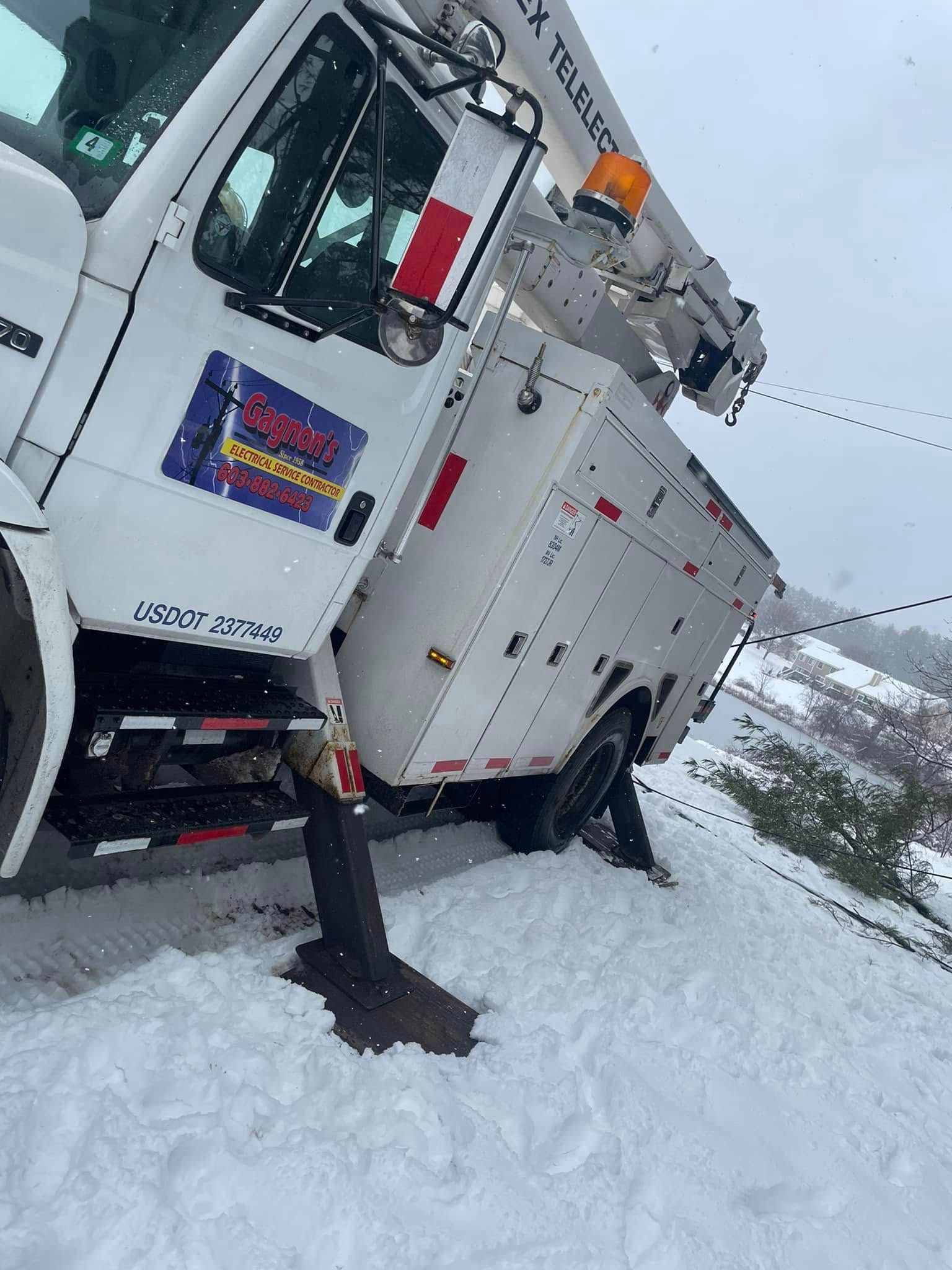 White utility truck stuck in deep snow on a snowy roadside, with mountains in the background