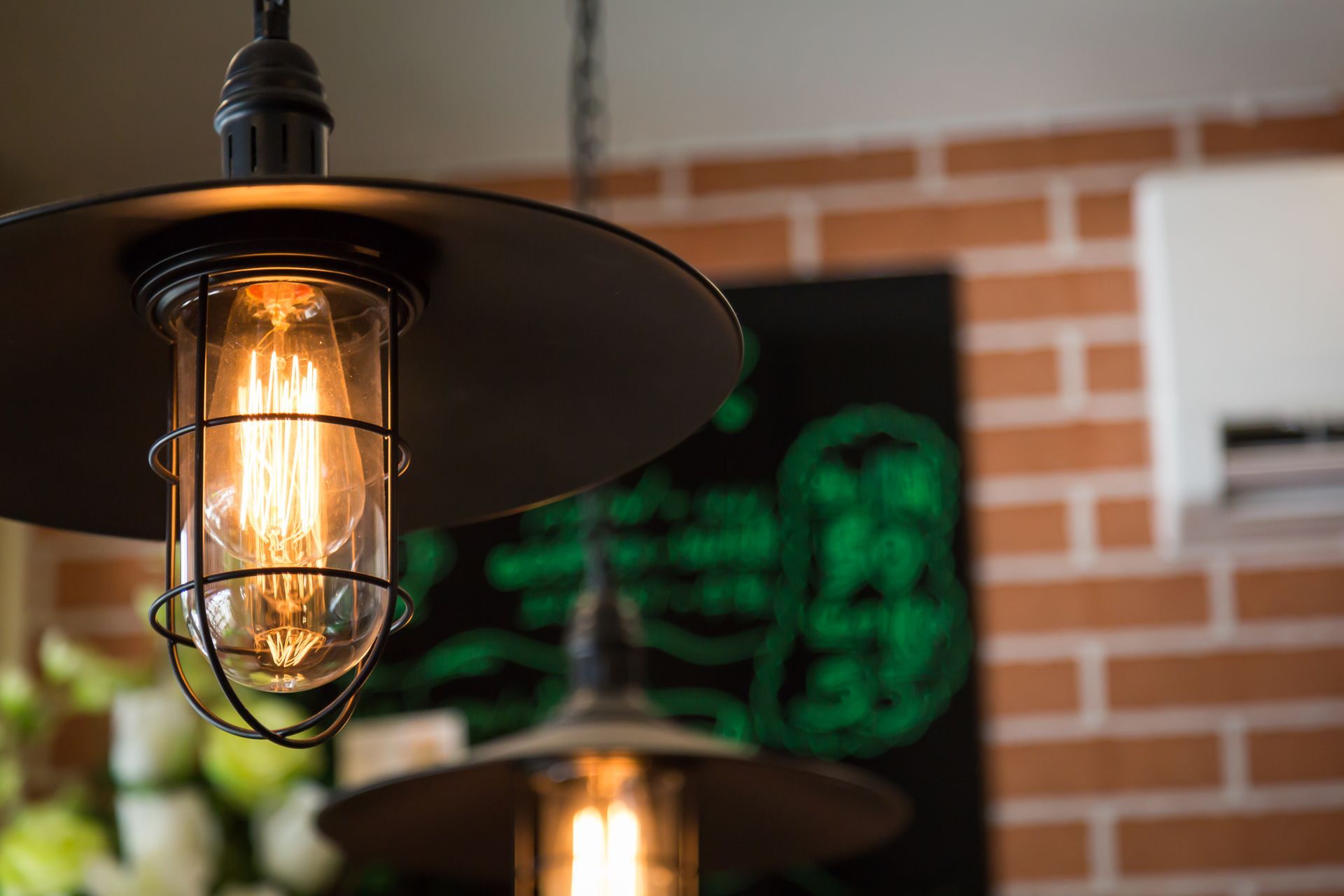 Outdoor patio heaters with glowing bulbs in front of a brick wall and green neon signage