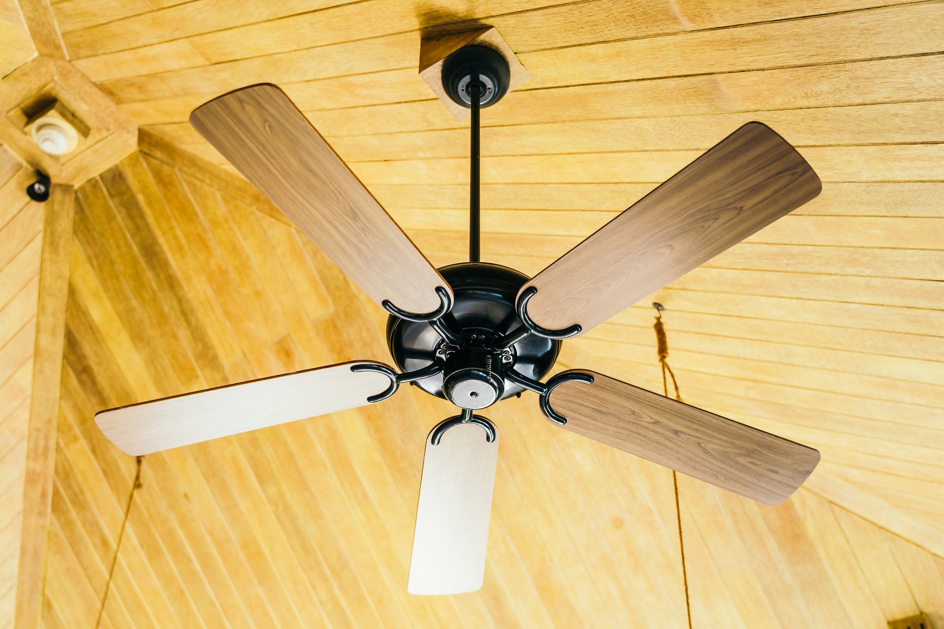 Ceiling fan with four wooden blades on a light wood paneled ceiling