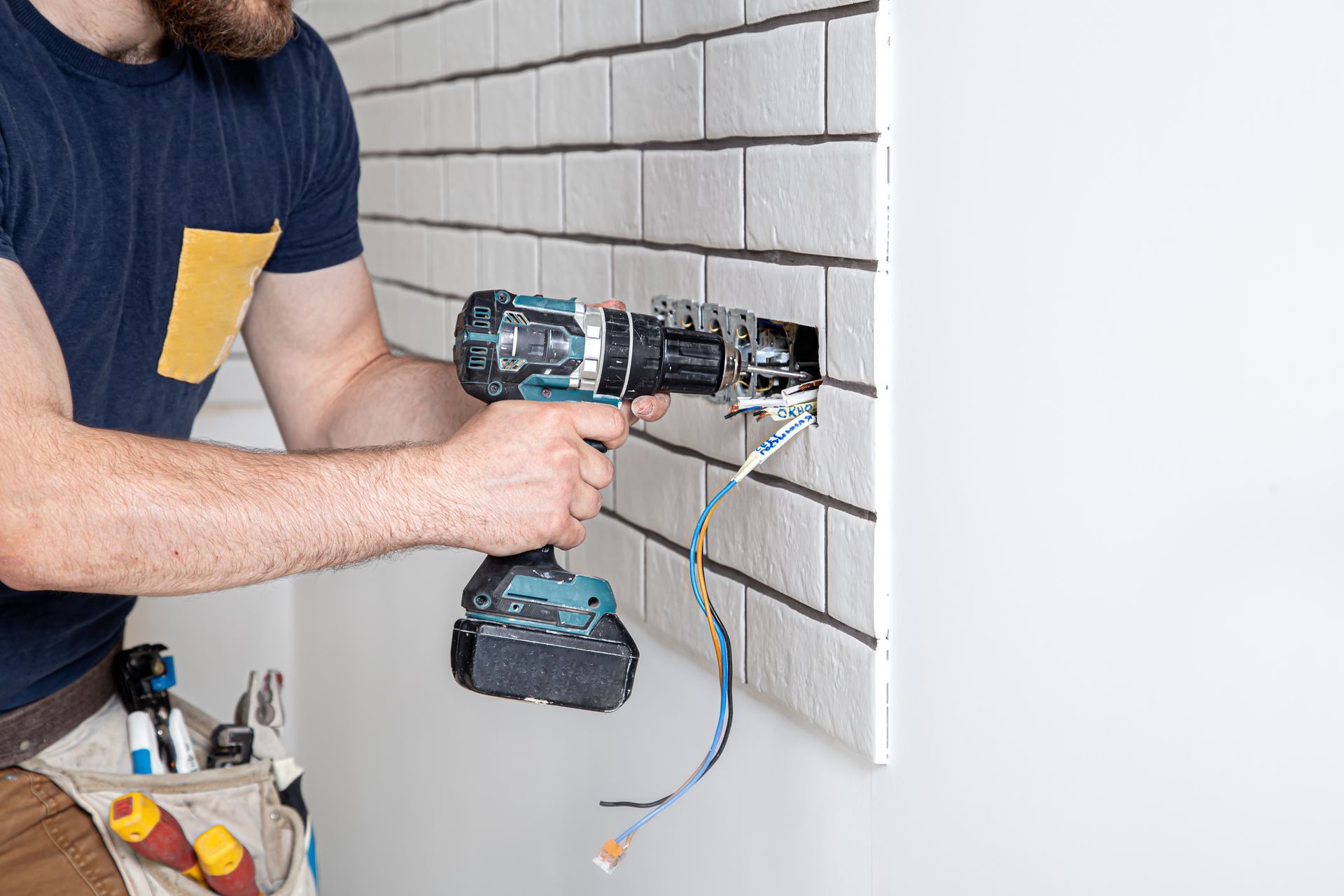 Person using a power drill to install a white tiled wall outlet box