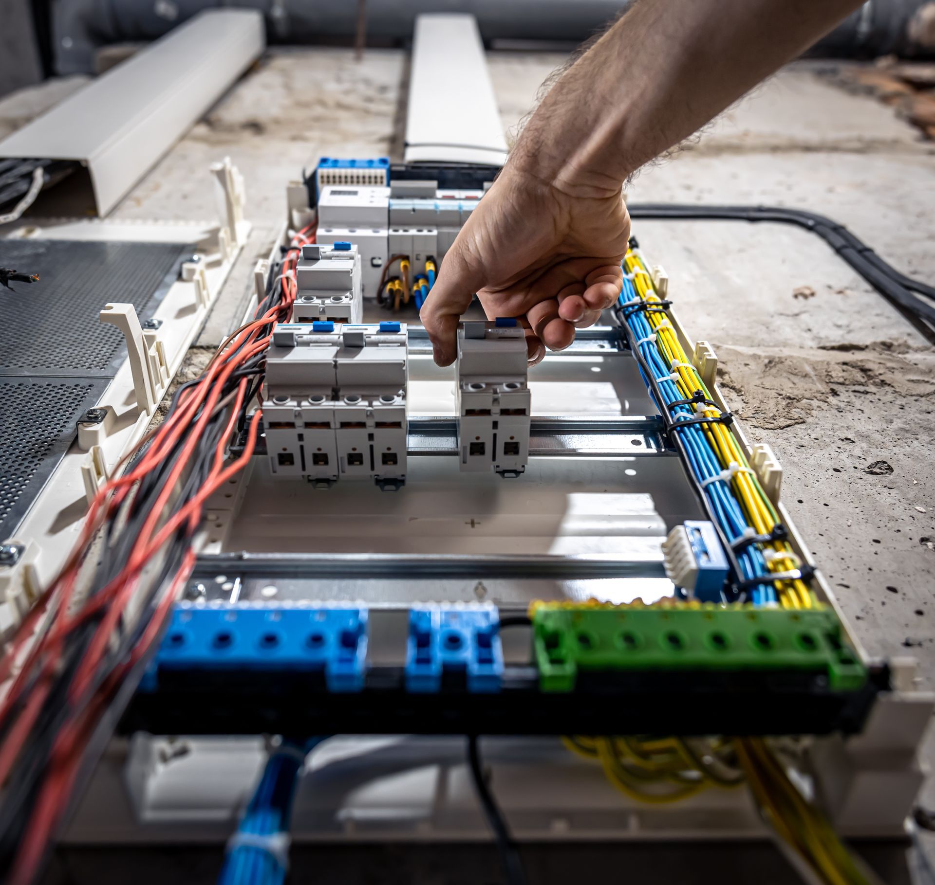 Hand placing a breaker into an electrical panel with red, blue, and green wiring