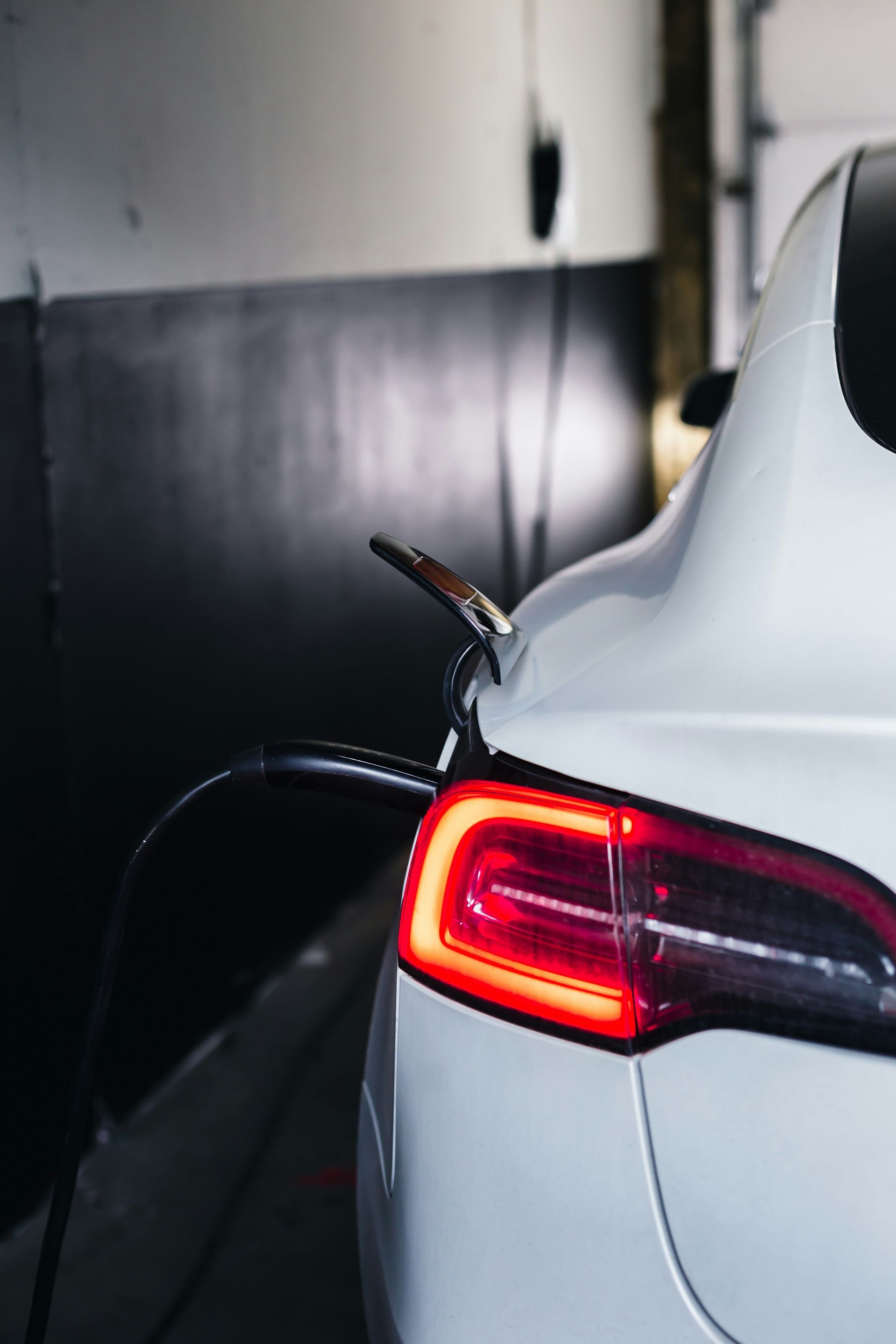 White electric car charging indoors, rear taillight glowing red