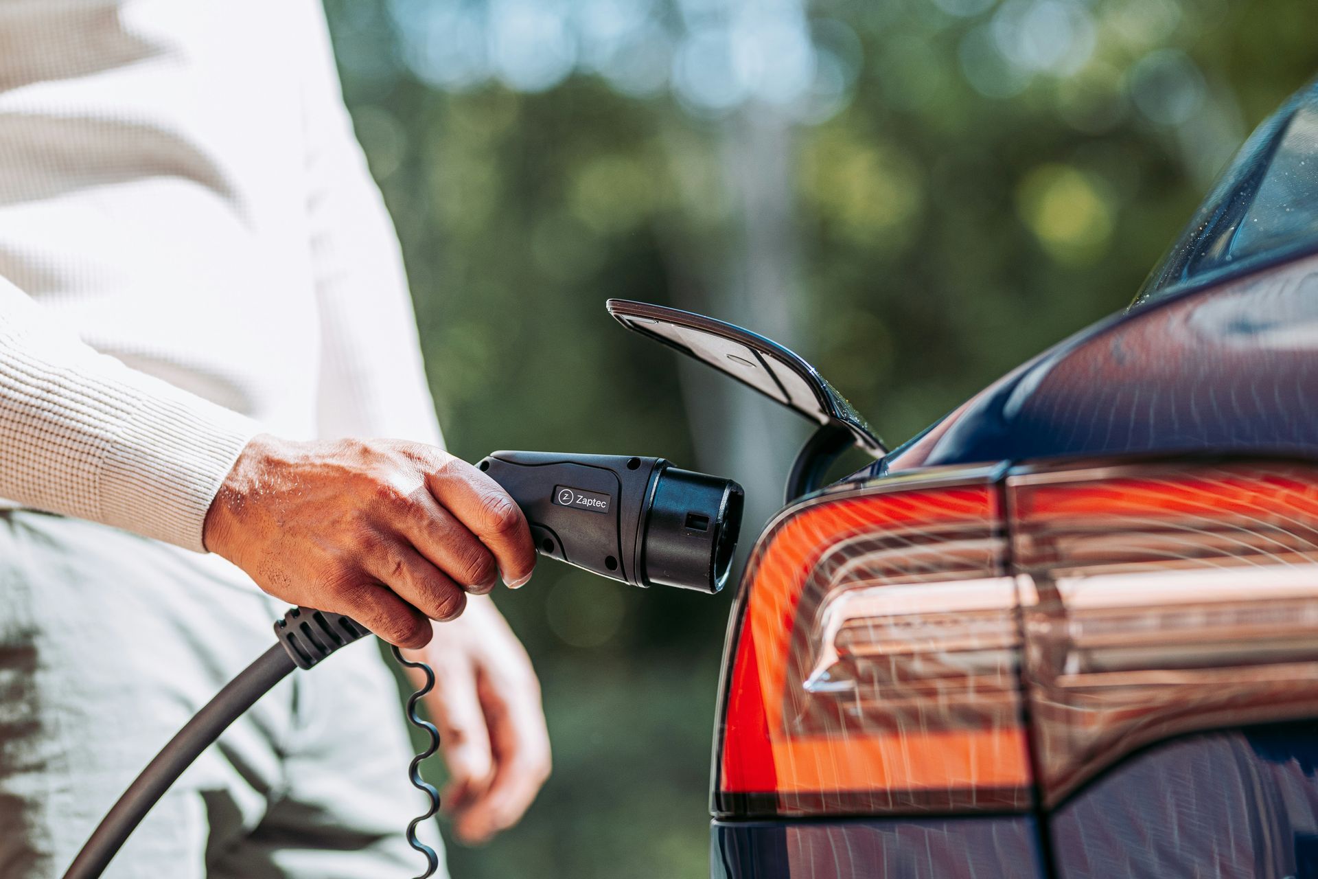 Person plugging a charging cable into a car’s rear charging port outdoors