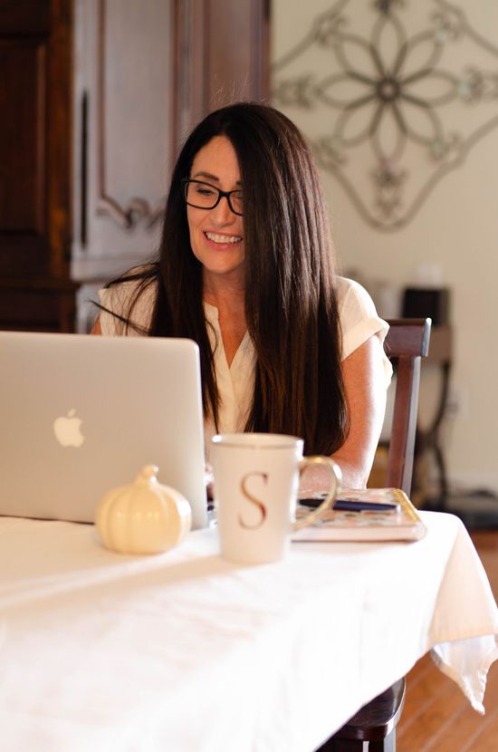 A woman is sitting at a table with a laptop and a cup with the letter s on it