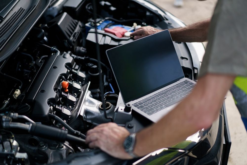 Person using a laptop to diagnose a car engine in an open hood repair scene — Precision Tuning in Bungalow, QLD