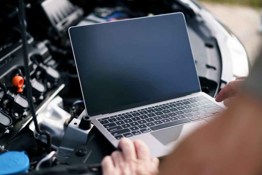 Person using a laptop to inspect a car engine in a garage — Precision Tuning in Bungalow, QLD