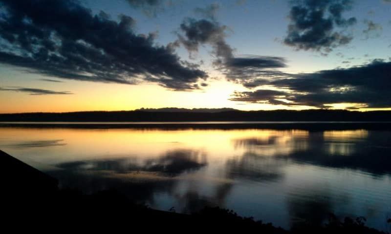 A sunset over a lake with a bridge in the distance