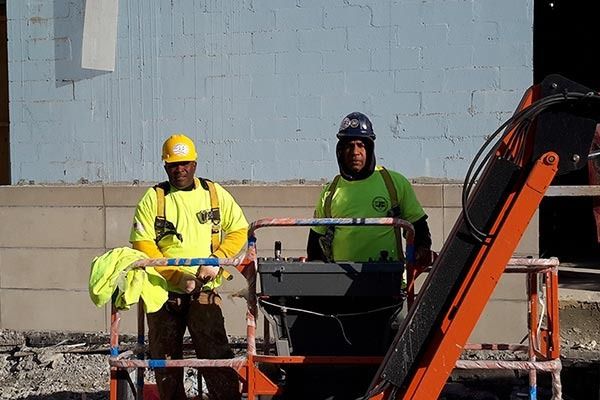 Two construction workers in neon green and yellow safety vests operate a lift.